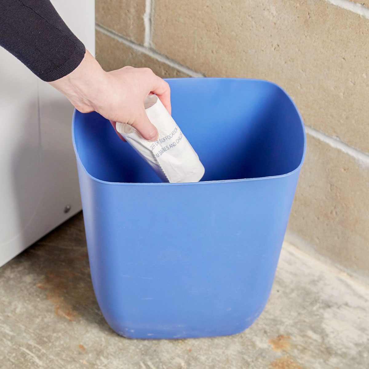 hand placing a roll of garbage bags at the bottom of a trash can