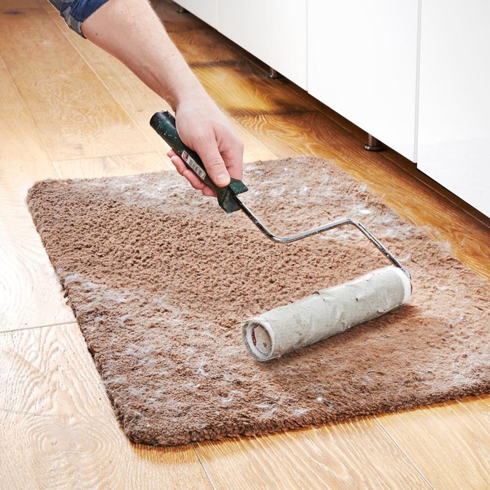 person using a paint roller with duct tape to remove pet hair from a small rug