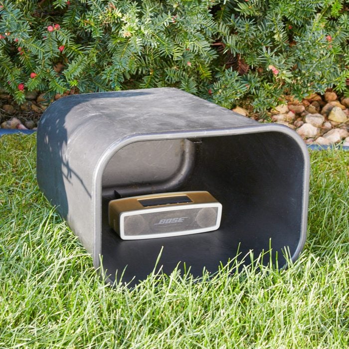 a trash can lying horizontally on a lawn with s bluetooth speaker inside