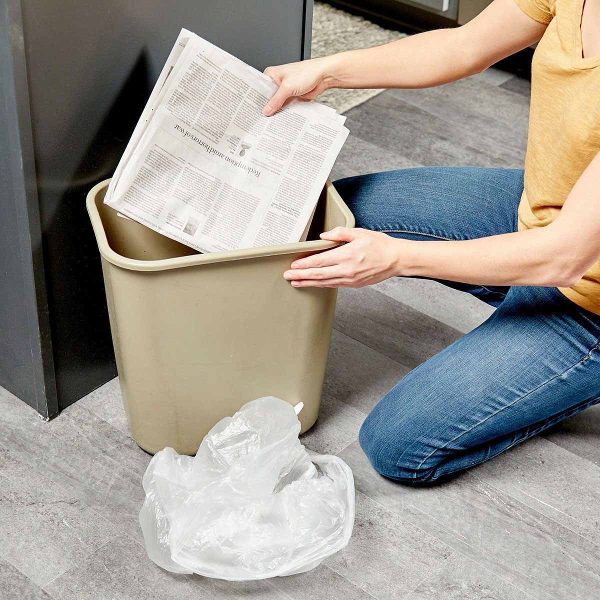 person putting newspaper in the bottom of a garbage can