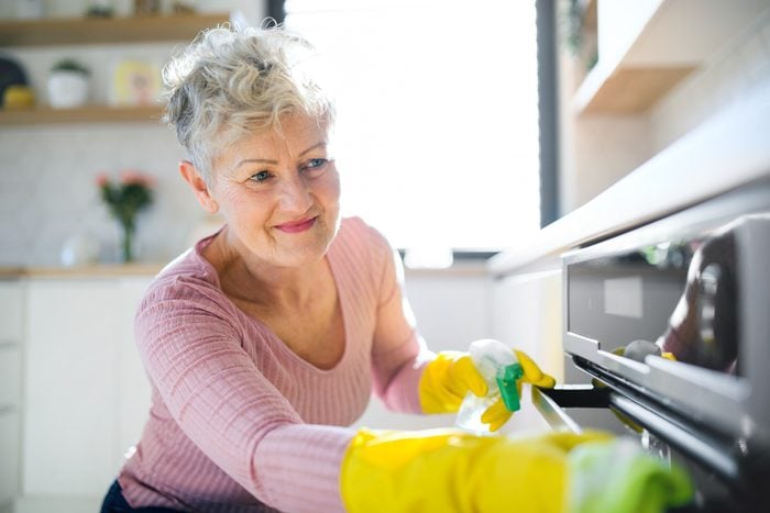 Front view of senior woman indoors at home, cleaning kitchen.