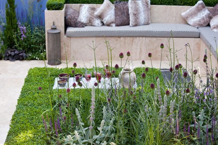 A contemporary, sunken Mediterranean garden made with terrazzo tiles and a terrazzo tile seating area with cushions for relaxing with a glass of wine.