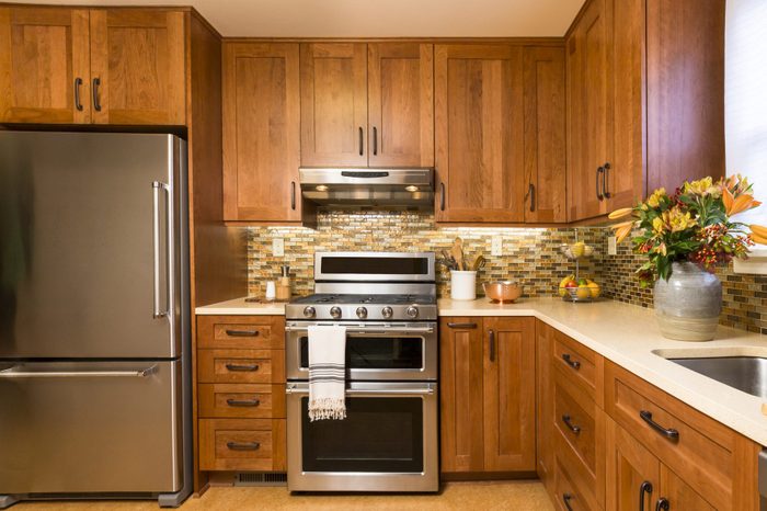 Contemporary mission style cabinet upscale home kitchen interior with cherry wood cabinets, quartz countertops, sustainable recycled linoleum floors & stainless steel appliances including refrigerator & gas stove