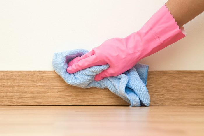 Employee hand in rubber protective glove with micro fiber cloth wiping a baseboard on the floor from dust at the wall. Spring general or regular clean up. Commercial cleaning company concept.