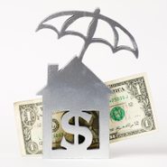 home sculpture with dollar sign and umbrella with dollar bill to represent homeowners insurance concept