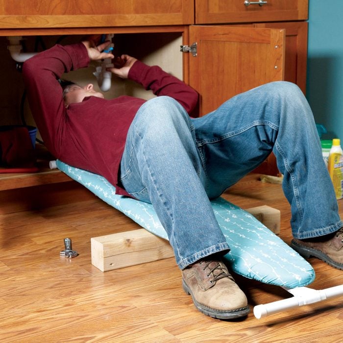 man laying on ironing board to repair under the sink