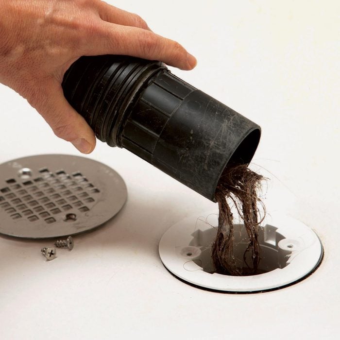 close up view of hand cleaning hair out of a bathtub drain