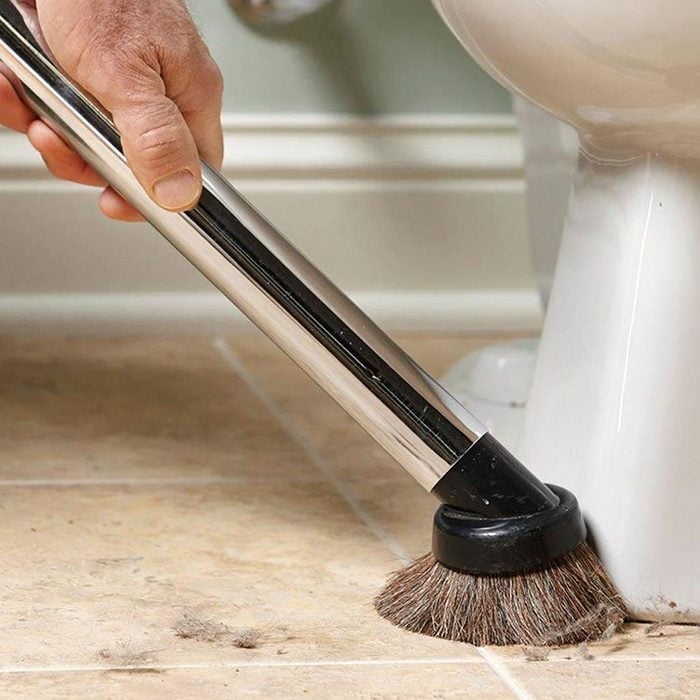 vacuuming the base of a toilet on a tile floor