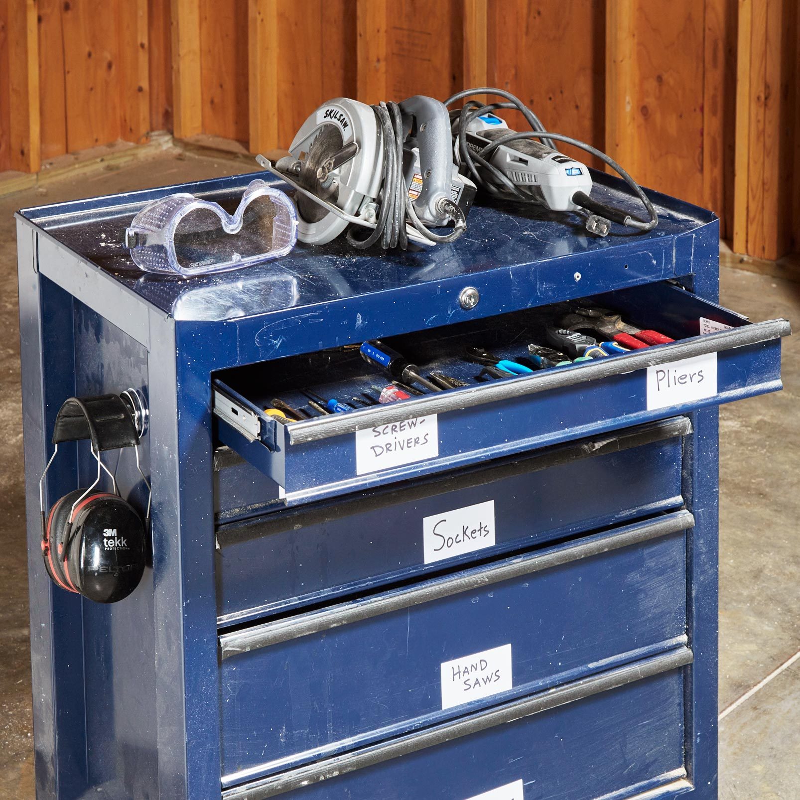 blue standing toolbox with an open drawer, safety googles and power tools on top and magnetic labels on each drawer