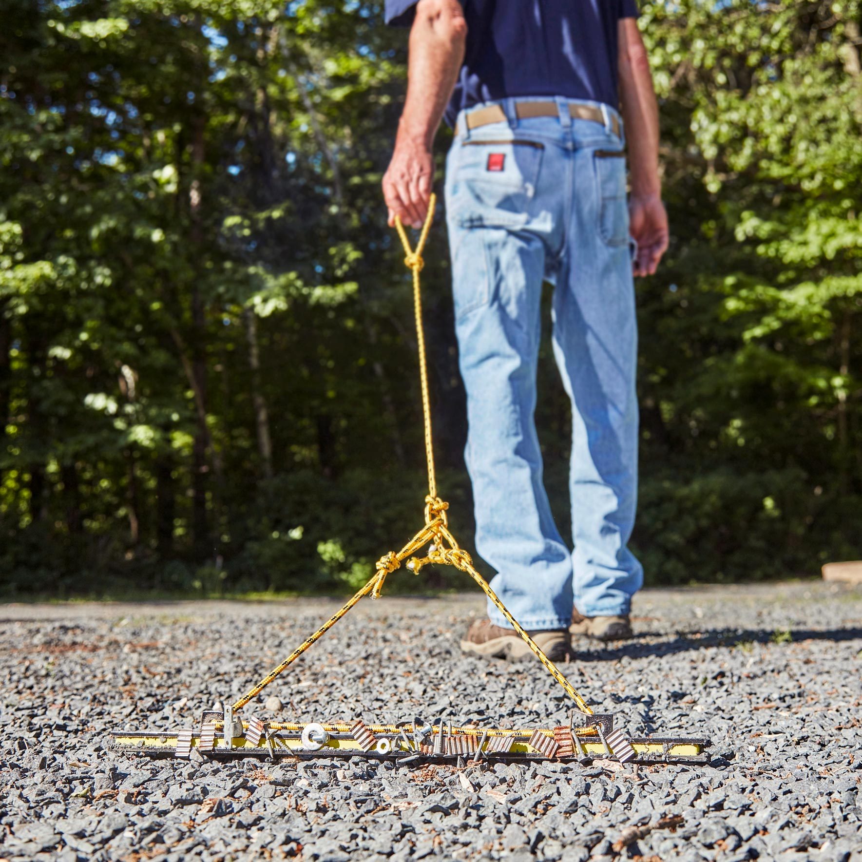 man with a magnetic rake picking up screws from a gravel driveway