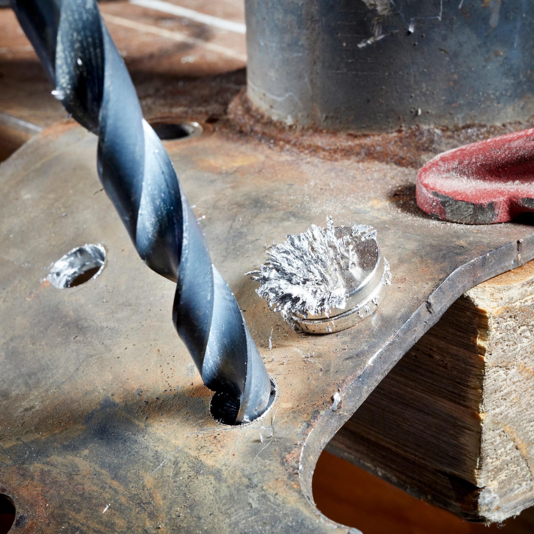 a large drill bit drilling a hole in metal with a magnet next to it to catch the shavings