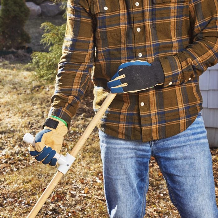 man in flannel shirt and jeans holding a PVC handle midway on a rake handle