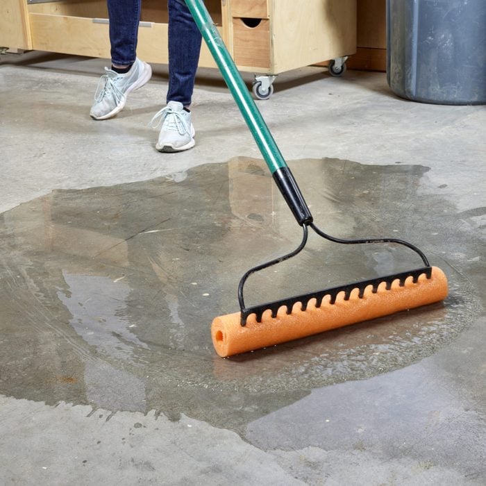 woman using a rack with a pool noodle attached to clean water on garage floor
