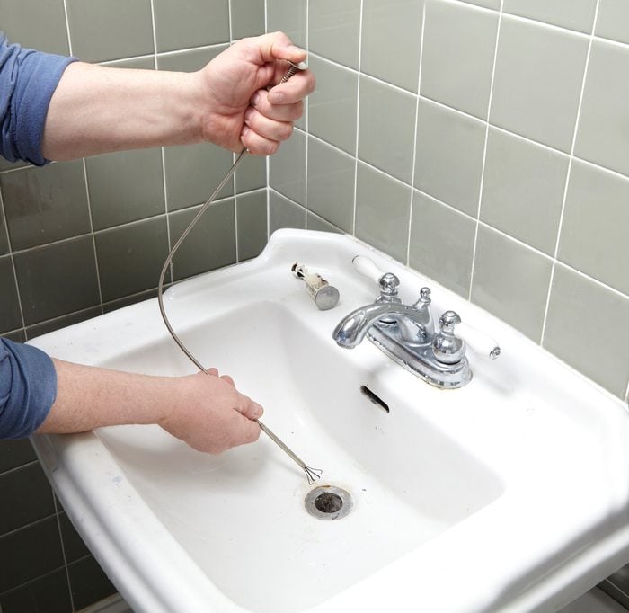 hands cleaning out bathroom sink drain
