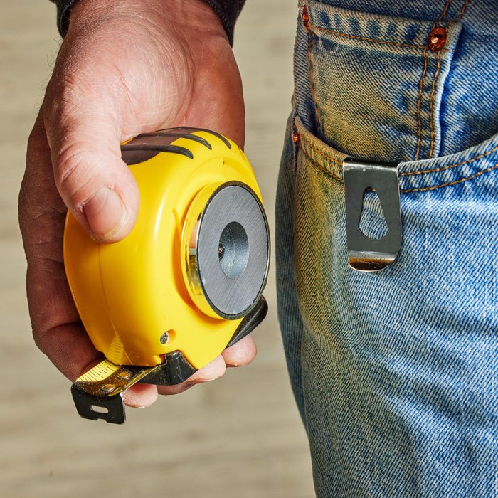 close up of a man holding a yellow tape measure next to a close up of his jean pocket with a clip