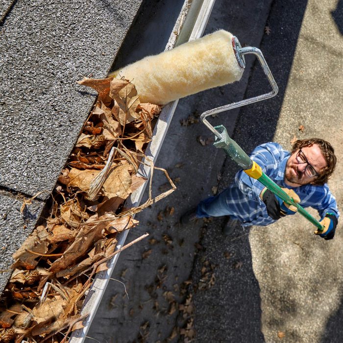 man cleaning leaves out of gutter with paint roller