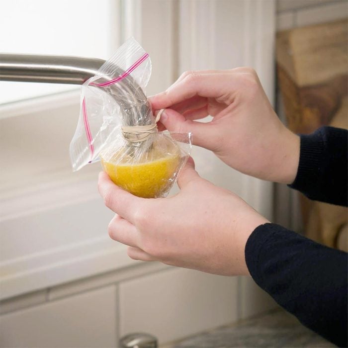 hands with a lemon in a bag around faucet to remove hard water buildup