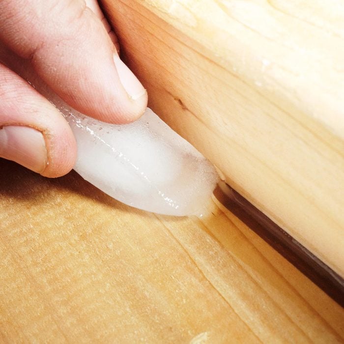 close up of hand holding and ice cube to apply caulk to between two pieces of wood