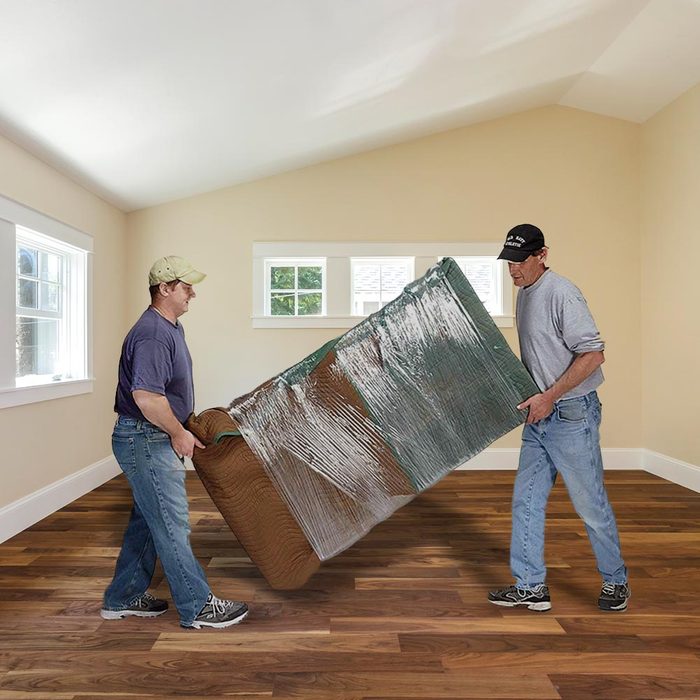 two men moving a couch wrapped up in a room with hardwood floors