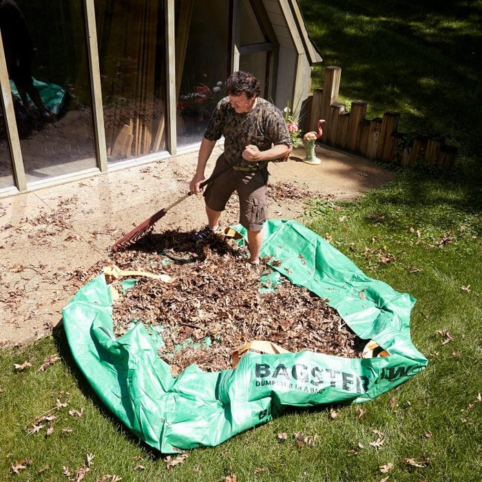 man cleaning up leaves in yard with a large tarp bagster