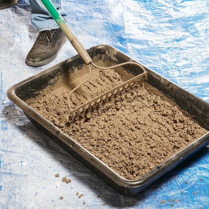 Mixing Concrete with a rake and tray on blue tarp
