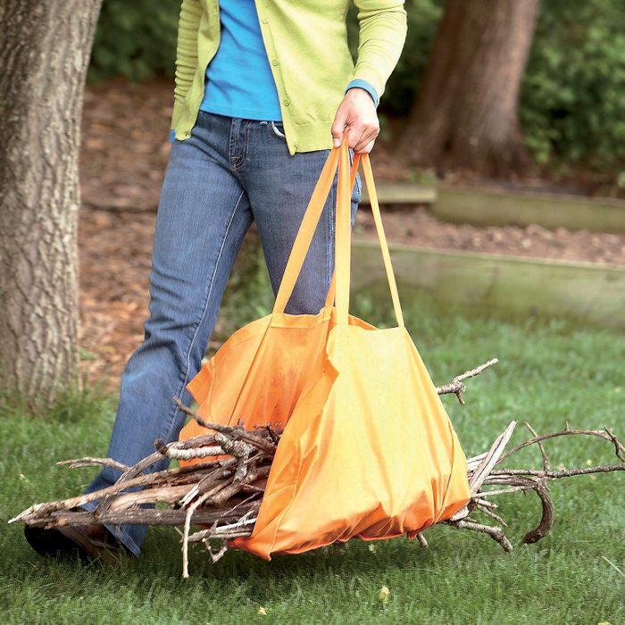 woman carrying a pile of sticks and branches in an orange carrying sling