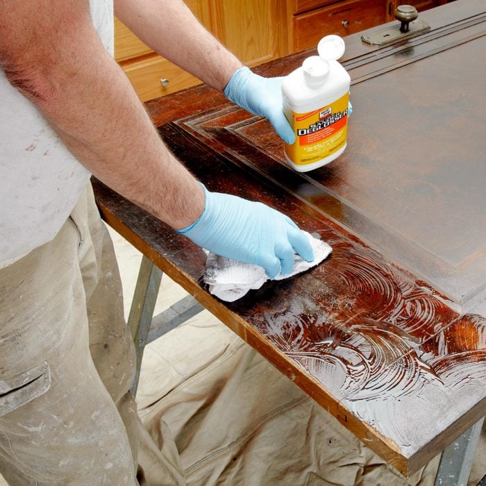 closeup of a person applying liquid sandpaper deglosser to an old door that has varnish on it