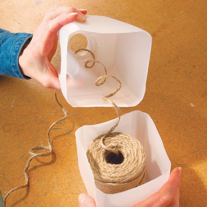 a spool of jute twine in the bottom of a milk jug cut in half with a string going through the top opening of the other half of the jug