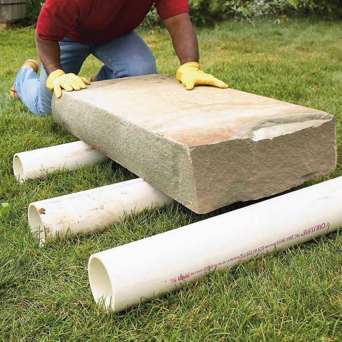 man with yellow gloves moving large piece of concrete by rolling it over PVC pipes