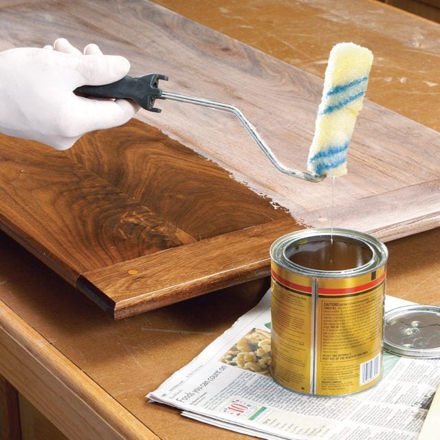 gloved hand applying stain with a paint roller