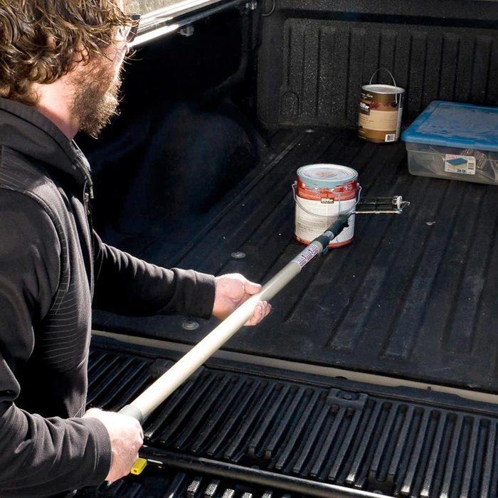 man using paint roller to get far away paint can in truck bed