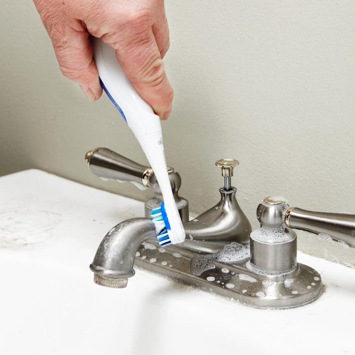 hand cleaning a sink faucet with a toothbrush