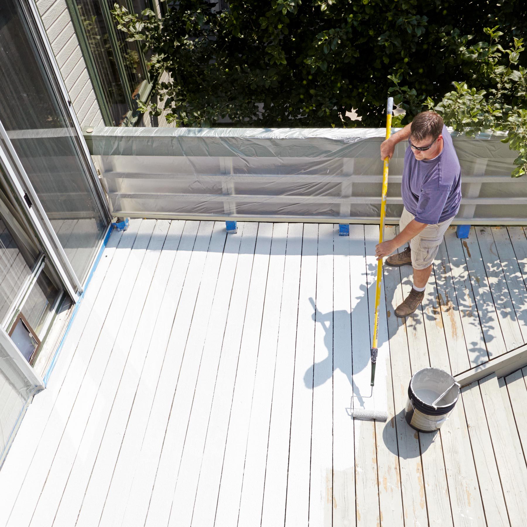 man restoring wooden deck with white paint