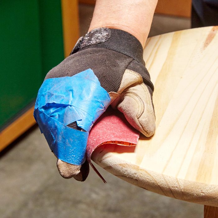person with gloves sanding the edge of a table
