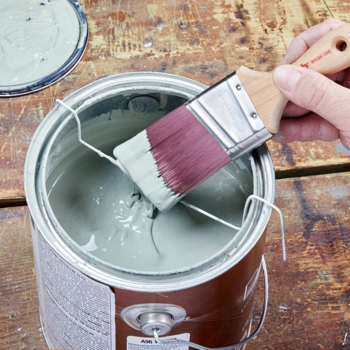 using a metal hanger to clean off paint brush in a paint can