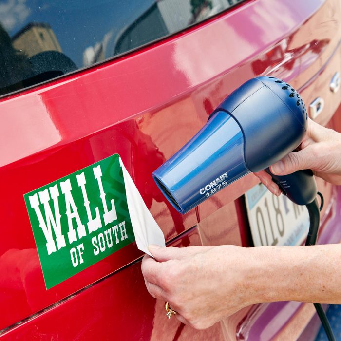 using a hair dryer to remove a bumper sticker from a car