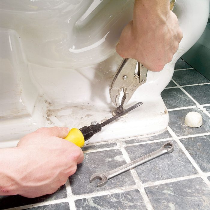 using a hacksaw to cut a stuck bolt from the base of a toilet