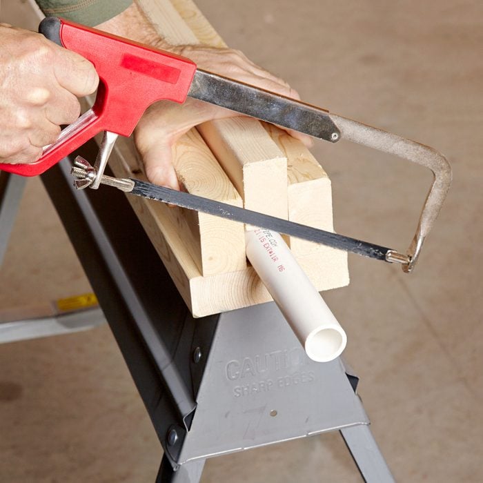 cutting a PVC pipe with a hacksaw and a homemade wooden holder