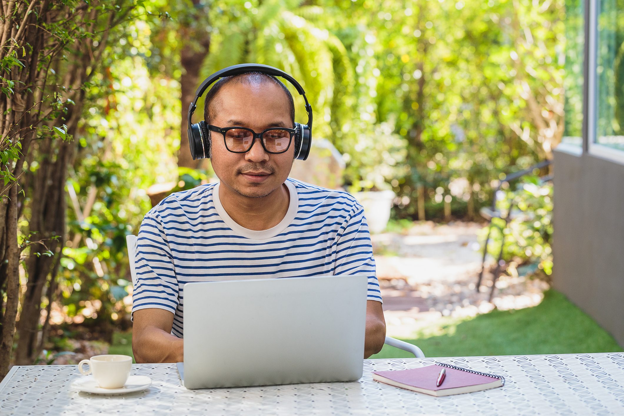 Asian mature men working with laptop computer and listening to music while setting in front or back yard outdoors at home