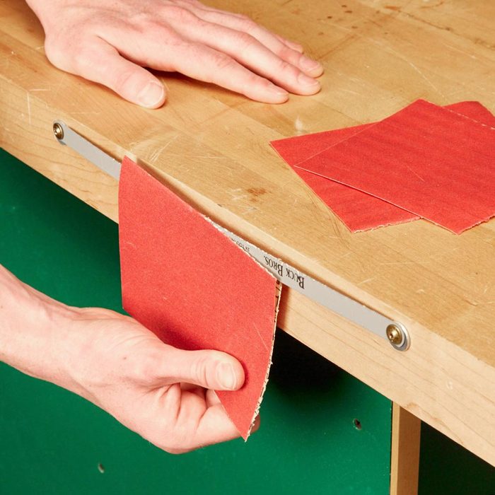 cutting sandpaper on a blade mounted on the edge of a table