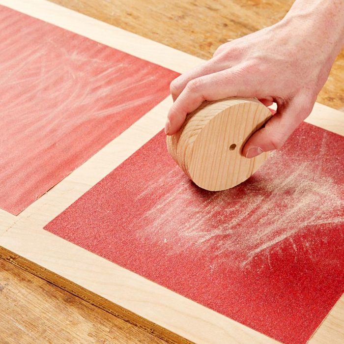 Sanding a small piece of wood on a sandpaper mounted to a larger piece of wood