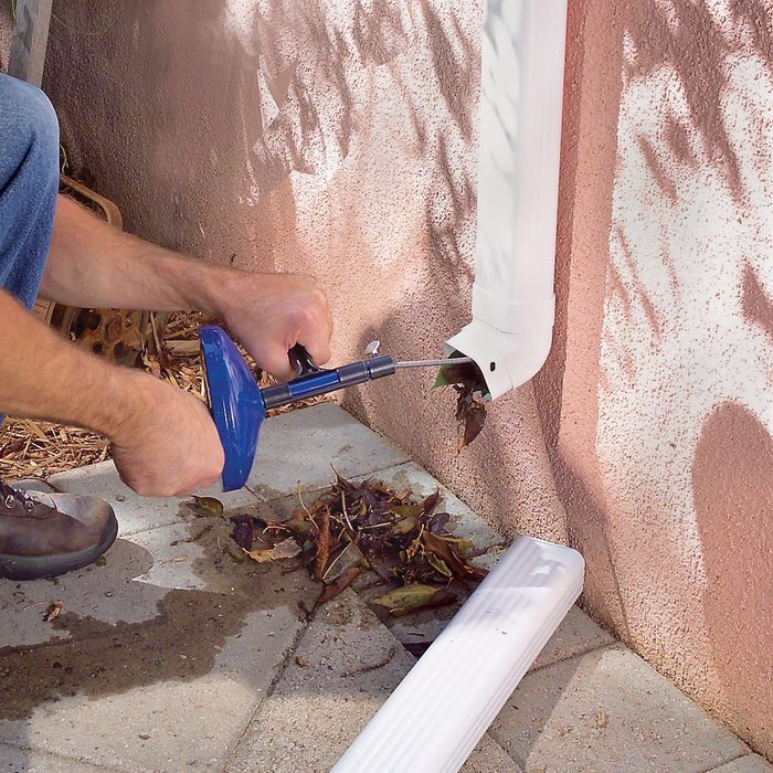 man cleaning out gutter downspout with a plumbing snake