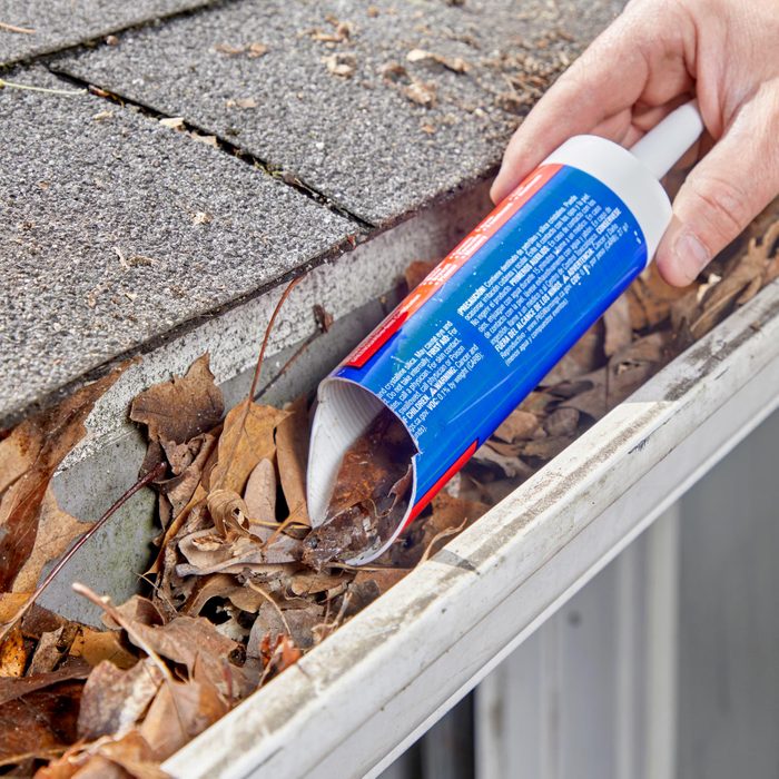 using a caulking tube to scoop out leaves in a gutter