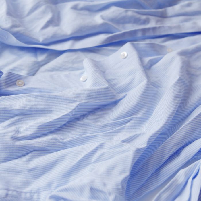 Blue cotton wrinkled and rumpled shirt on white. Washed shirt after tumble dryer