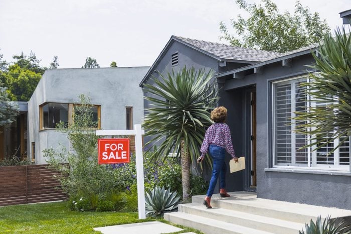 Female real estate agent carrying document while walking into house with a for sale sign out front
