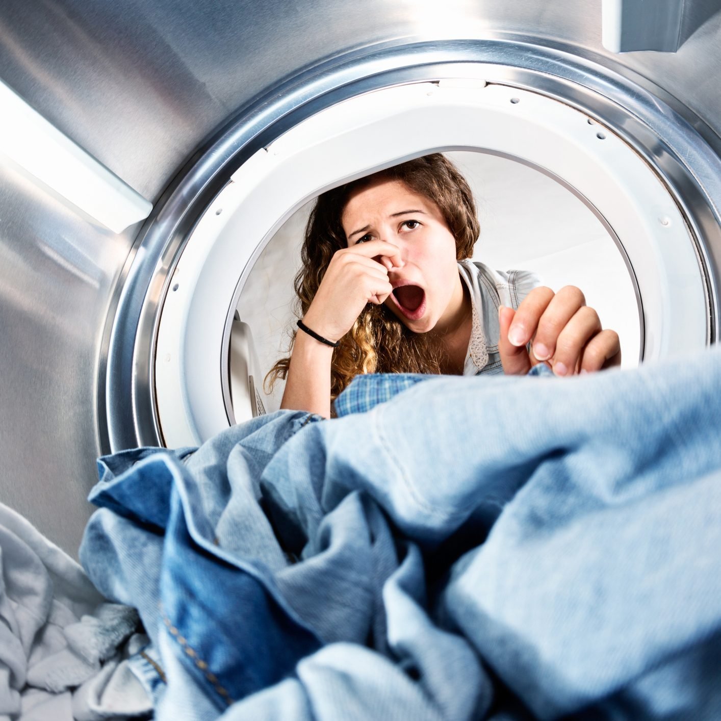 Laundry Left In Clothes Dryer Stinks! Unhappy Woman Holds Nose.