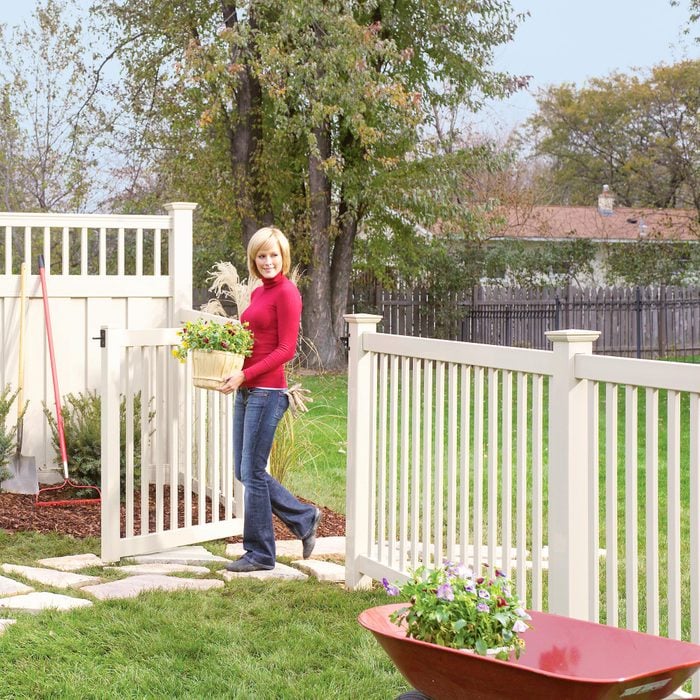 woman carrying flowers through the gate of a Vinyl Fence in the backyard