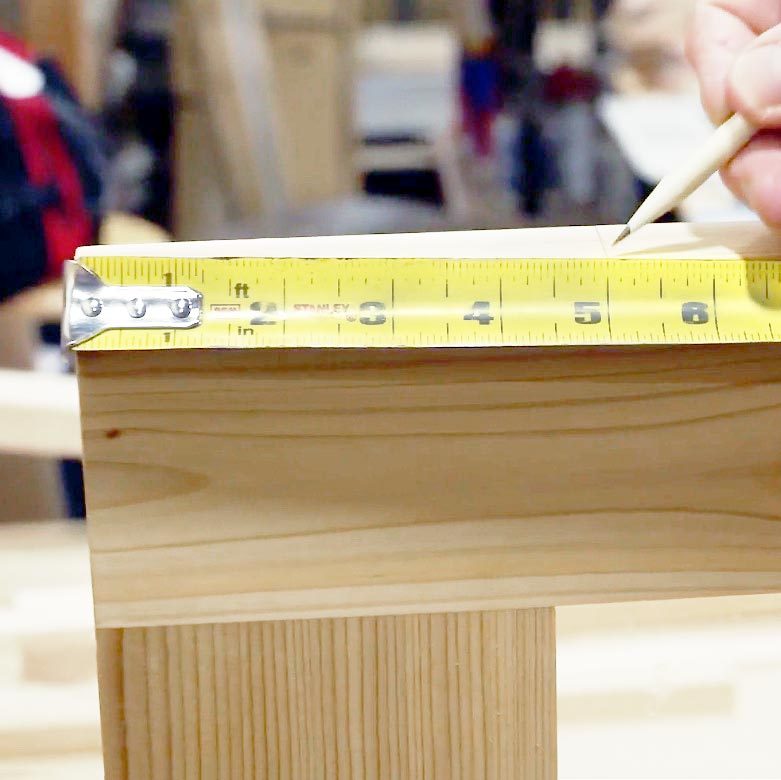 close up of a a tape measure and a hand using a pencil to mark the measurement on the wood