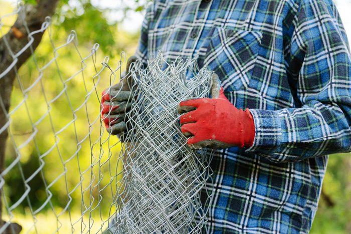 close up of hands with red gloves unrolling chain link fence for install