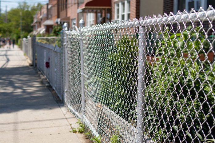 Chain Link Fence along an Empty Sidewalk with a Row of Old Homes in Astoria Queens New York